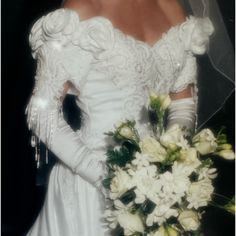 a woman in a white wedding dress holding a bouquet of flowers and wearing an elaborate veil