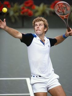 a man swinging a tennis racquet at a ball on a court with flowers in the background