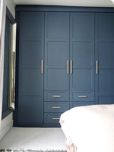 a bedroom with dark blue cabinets and white sheets on the bed in front of it