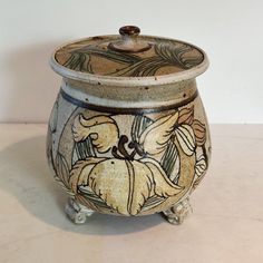 a ceramic pot with an artistic design on the lid sitting on a white table top