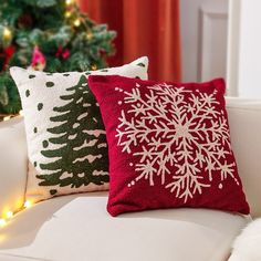 two christmas pillows sitting on top of a couch next to a christmas tree with lights