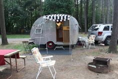 a camper trailer is set up in the woods with chairs and an open fire pit