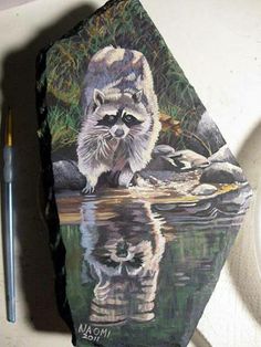 a painting of a raccoon on a rock next to a pen and paper