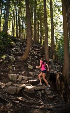 a woman is running up some rocks in the woods