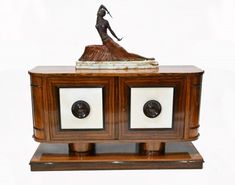 an old fashioned wooden cabinet with a statue on it's top and two knobs