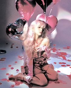 a woman sitting on the ground with heart shaped balloons in front of her head and hands