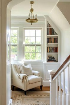 a white chair sitting under a window next to a book shelf