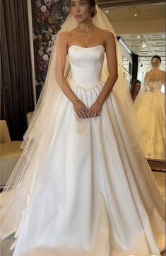 a woman standing in front of a wedding dress with her hands on her hips and looking at the camera