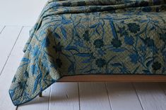 a blue and green bedspread on a bed with white wood floors in the background