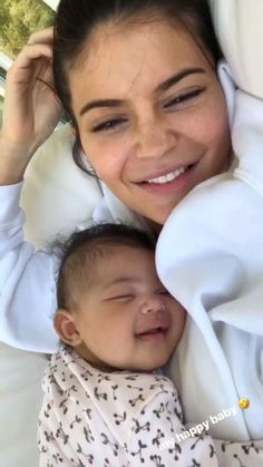 a woman holding a baby in her arms while laying on top of a white blanket