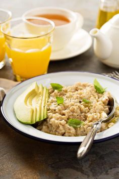 a bowl of oatmeal with an avocado on the side and cups of orange juice in the background