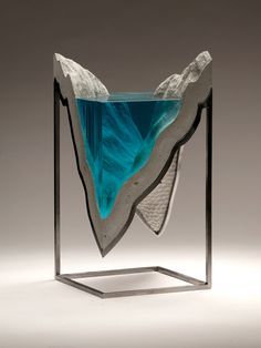 a glass sculpture with blue and white water in it's center, sitting on a metal stand