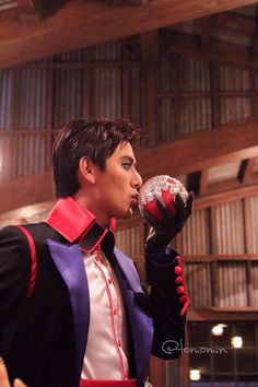 a man in costume drinking from a red and black glass bottle while standing next to a wooden paneled wall