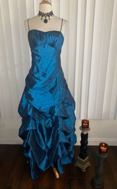 A stunning gown down in a taffeta like fabric and almost turquoise blue color. It is sleeveless with a fitted bodice and a long gathered skirt. This gown has pleating on the bust as well as cups on the inside. It zips as well as laces up and ties in back. Truly beautiful. Pair it with black velvet accessories and let it take your breathe away. *choker not included *Era: 2000's *Label: Sally USA *Fabric: Feels and looks like taffeta however I do believe this may be a poly type blend *Condition: Gently worn / No Flaws *Size: I believe this best fits a L but please see measurements below *Bust: 18 inches *Waist: 17 inches. Please keep in mind that it laces up the back and you may be able to pull it in a bit more. *Hips: 22 inches *Length: 55 inches Blue Evening Dress With Corset Back And Fitted Bodice, Blue Evening Gown With Corset Back, Evening Blue Gown With Corset Back, Blue Ball Gown With Corset Back For Prom Season, Blue Ball Gown With Corset Back For Prom, Taffeta Ball Gown Evening Dress For Prom, Fitted Blue Gown With Lined Bodice, Taffeta Ball Gown For Prom Season, Floor-length Taffeta Ball Gown For Prom Season