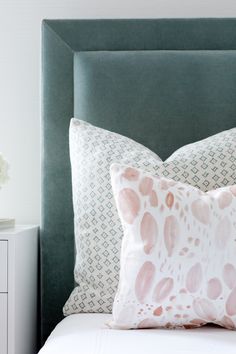 a green headboard with pink and white pillows on it next to a night stand