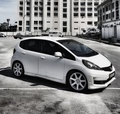 a small white car parked in a parking lot next to a tall building with lots of windows