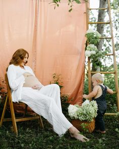 a pregnant woman sitting in a chair next to a toddler holding a flower pot