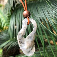 a marble sculpture hanging from a palm tree with a wooden bead in the middle