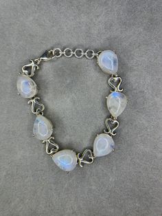 This is a beautiful natural Rainbow Moonstone Sterling Silver Bracelet that yields approximately 70 carts of Moonstone. The Moonstone are pear shape and the bracelet measures 7 inches and has a 1 inch extender. The bracelet is set in sterling silver and weighs a hefty 25 grams. Moonstone is known for aiding fertility, enhancing patience, and it enhances feminine energy. The Moonstones originated in Sri Lanka and the bracelet has a pattern of hearts between each moonstone. Elegant Moonstone Gemstone Bracelets, Elegant Moonstone Gemstone Bracelet, Elegant White Moonstone Crystal Bracelet, Elegant Pear-shaped Moonstone Jewelry, Gemstone Moonstone Bracelets, Elegant Round Moonstone Crystal Bracelet, Adjustable Elegant Sterling Silver Bracelet With Moonstone, Adjustable Elegant Sterling Silver Moonstone Bracelet, Elegant Adjustable Sterling Silver Moonstone Bracelet