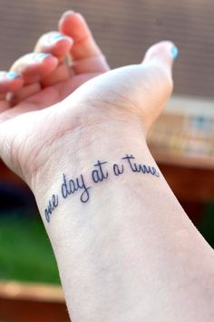 a woman's wrist with the words one day at a time tattooed on it