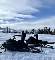 two people standing next to a snowmobile in the snow