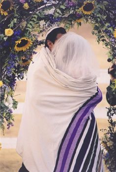 a woman wearing a white shawl under a floral arch