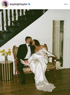 a bride and groom sitting on a chair in front of a stair case, kissing