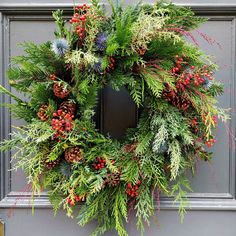 a christmas wreath hanging on the front door with pine cones and evergreens around it