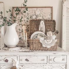 a white dresser topped with baskets filled with dishes and candle holders on top of it