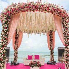 an outdoor wedding ceremony setup with pink and white flowers on the altar, couches, and drapes