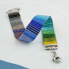 two colorful bracelets sitting next to each other on top of a white table with a metal keychain