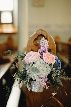 a vase filled with flowers sitting on top of a wooden table next to a church pew