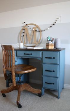 a blue desk with a wooden chair and letter m on the wall above it,