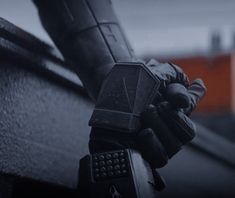 a person wearing gloves and holding a cell phone on top of a wooden roof with buildings in the background