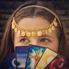 a woman holding up four cards in front of her face with gold chains around her head