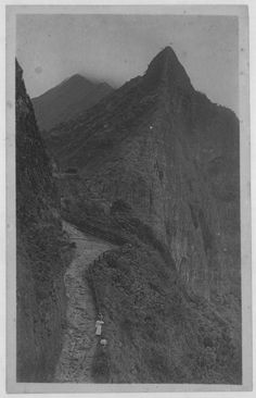 an old black and white photo of a man walking on a path in the mountains