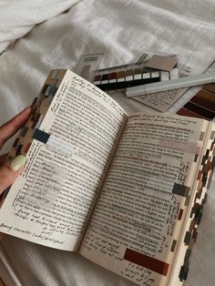 an open book sitting on top of a bed next to some pens and pencils