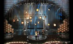 two people standing on stage in front of an auditorium with chandeliers and lights