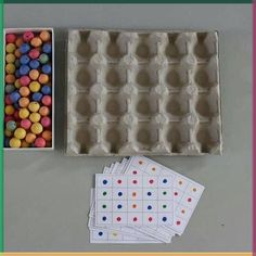 an egg carton filled with lots of different colored candies next to some cards