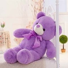 a large purple teddy bear sitting on top of a bed next to a white headboard