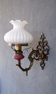 a wall light with a white glass shade hanging from it's side on a gray wall