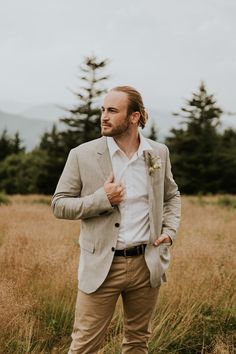 a man standing in the middle of a field wearing a blazer and tan pants