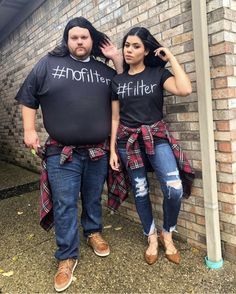 a man and woman standing next to each other near a brick wall wearing matching shirts