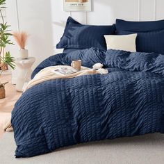 a bed with blue comforter and pillows in a room next to a potted plant