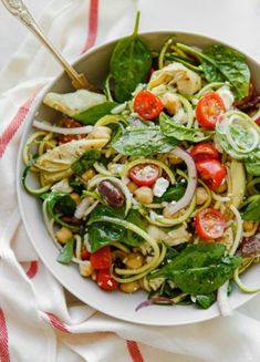 a white bowl filled with pasta and veggies on top of a red and white towel