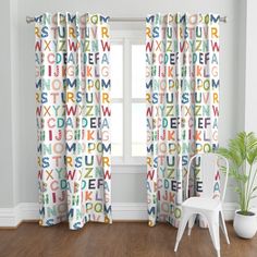 a white chair sitting in front of a window covered in colorful alphabet curtain valances