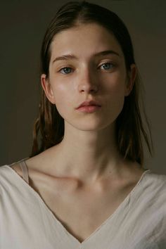 a woman with blue eyes is looking at the camera while wearing a white shirt and standing in front of a gray background