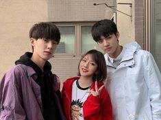 three young people standing next to each other in front of a building with one pointing at the camera