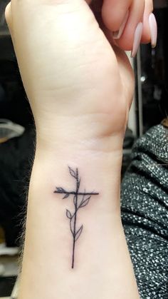 a small cross tattoo on the wrist with a single flower at the center and an arrow in the middle