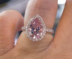 a close up of a person's hand with a pink diamond ring